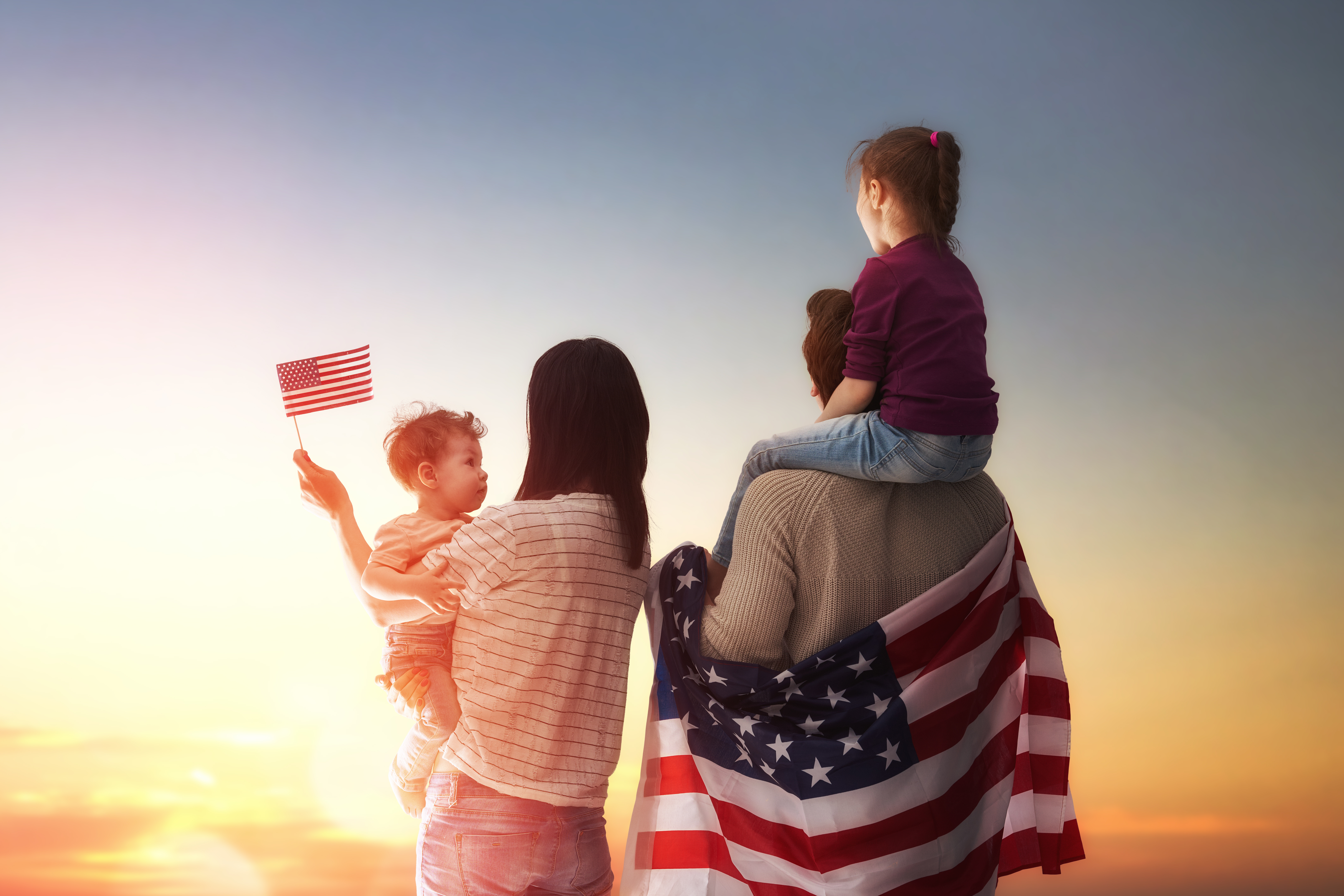 Family of four (husband, wife, daughter, son) looking out into the sunset, with American flags