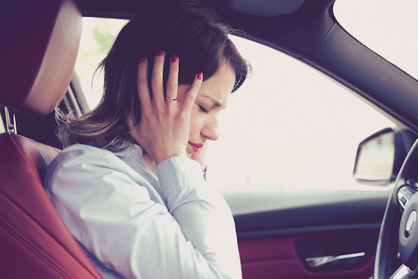 Woman frustrated with her hands covering her ears, sitting in driver's seat