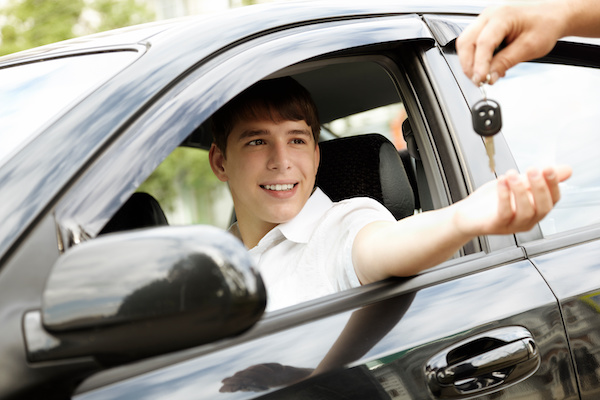 Young man receiving a pair of keys while sitting inside black vehicle