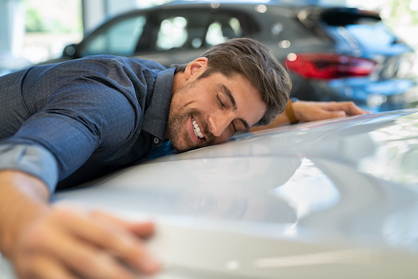 Man happily leaning against hood of a white vehicle, smiling relaxed