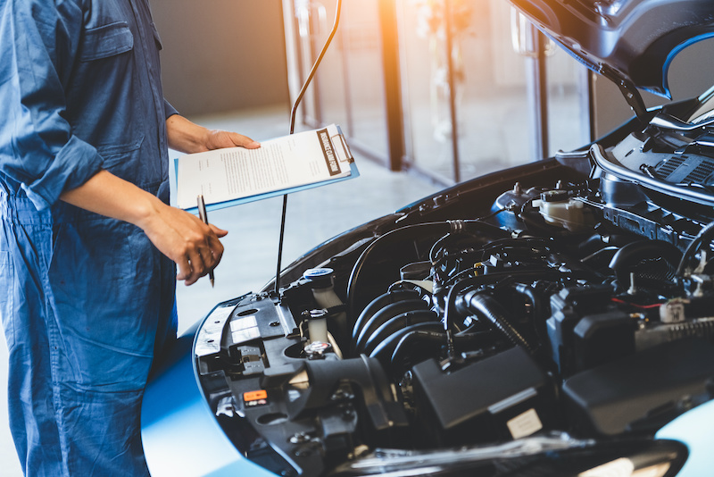 Auto Repair Staff inspecting an engine of a vehicle, holding clipboard and pen