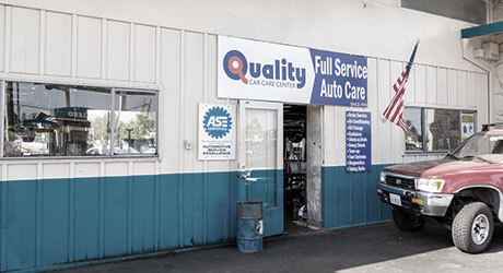 Red vehicle parked close to door leading to inside Quality Tune-Up Car Care, showing ASE Certified logo and American flag