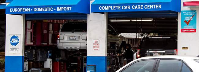 Light gray car parked outside of shop while repairs of two vehicles continue inside shop | Quality Tune-Up Auto Care