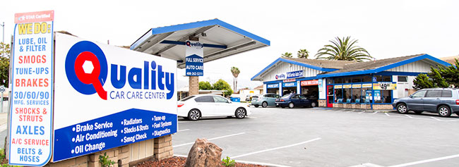 Outside of shop with sign indicating services on left side, vehicles parked | Quality Tune-Up Auto Care