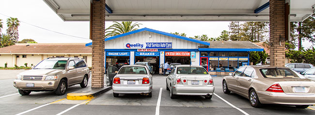 Row of vehicles parked in parking lot of shop, view of the shop in the background | Quality Tune-Up Auto Care