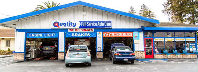 Outside of shop showing garages and vehicles in progress of repairs, with vehicles parked | Quality Tune-Up Auto Care