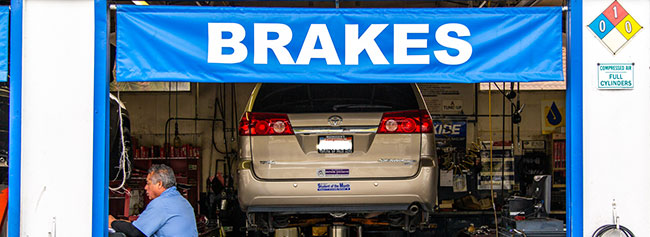 Up close of tan van lifted up with four tires laid below, staff member in progress of repairs | Quality Tune-Up Auto Care